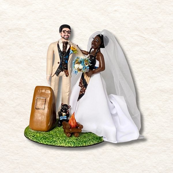 Imagem de uma figura decorativa de um casal de noivos em estilo artesanal, com detalhes de vestido de noiva e fato de noivo, em uma base de grama com elementos decorativos.